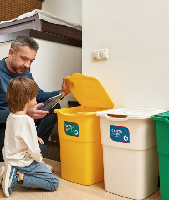 Cropped mother near father teaching little son throwing bottle in dustbin for glass at home. Ecological garbage recycle. Parenting. Young caucasian family spending time together. Domestic lifestyle
