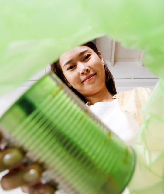 asian woman putting and sorting plastic aluminum can waste to recycle bin POV. Low angle view from inside green recycling bag.